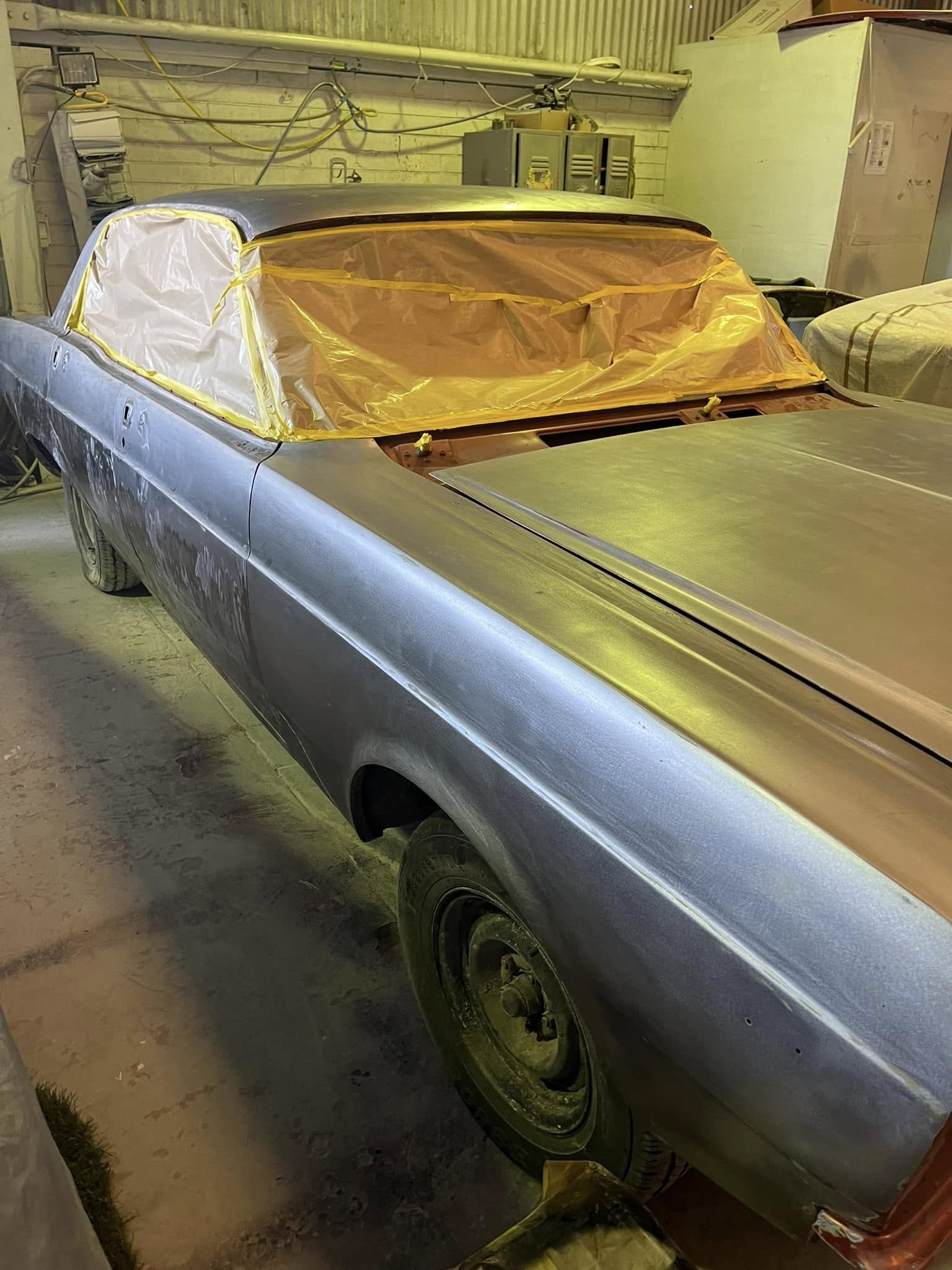 Classic car body in primer with windows masked in a workshop